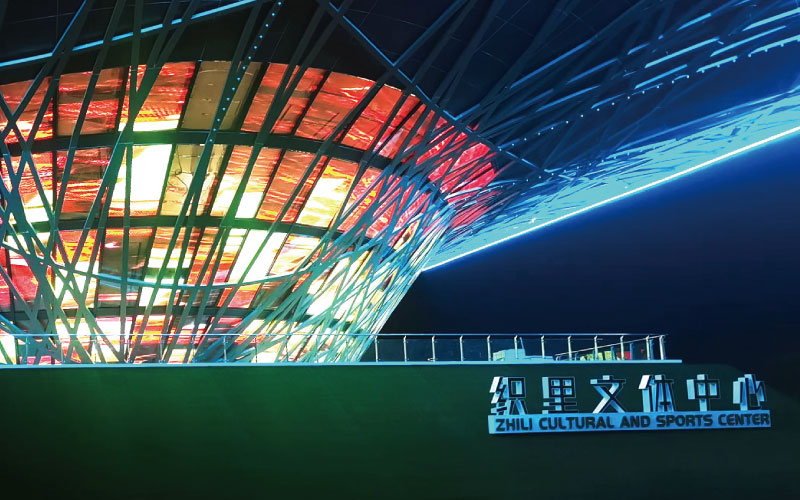 位于浙江湖州的織里文體中心,是一座大型異形鋼架結構建筑。三思為其定制近1000平米透明屏,運用高清LED透明屏及控制系統,將其打造成了一幅巨型建筑媒體立面。 位于浙江湖州的織里文體中心,是一座大型異形鋼架結構建筑。三思為其定制近1000平米透明屏,運用高清LED透明屏及控制系統,將其打造成了一幅巨型建筑媒體立面。